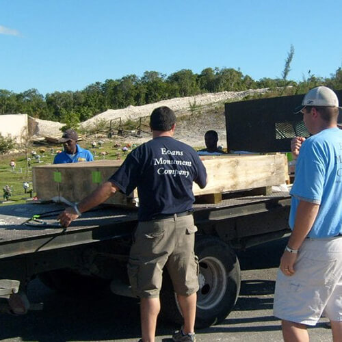 Evans Monument Company crew unloading a granite monument from a flatbed truck at a cemetery