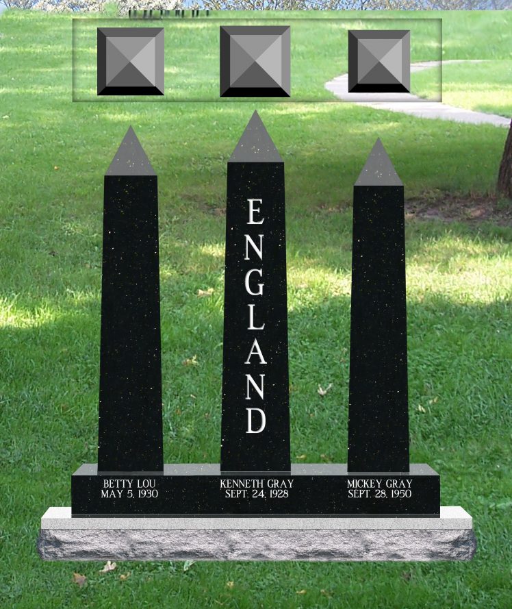 Three black granite obelisks with grey pyramid caps standing on one shared base