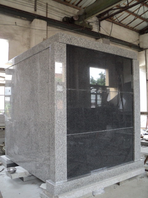 A finished walk-in granite mausoleum in grey and black, photographed in the fabrication shop