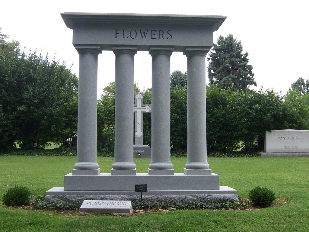 Large granite estate monument with four columns and a carved cross, standing on a cemetery lawn