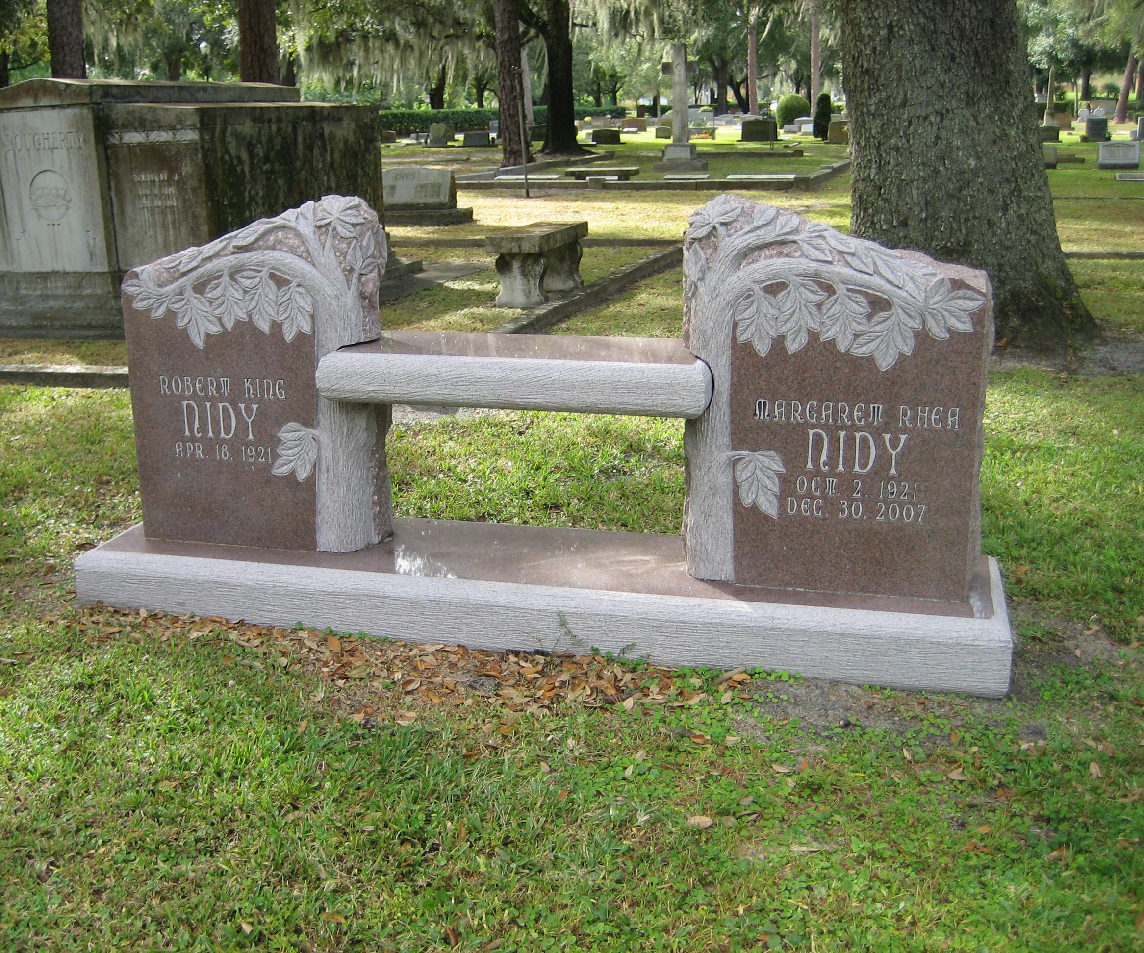 Rose granite companion bench memorial with carved leaves and branches, standing under oak trees in a cemetery